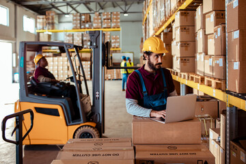 Warehouse Worker Using a Laptop Amidst Stacked Boxes