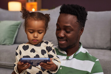 Portrait of young Black father and daughter using smartphone together for supervised screen time