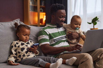 Portrait of young working father with two children using laptop and smiling enjoying parenting, copy space - obrazy, fototapety, plakaty