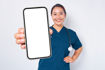 Fototapeta na wymiar Smiling young Asian woman nurse working wearing a blue uniform showing smartphone with blank screen isolated on white background. Healthcare medicine concept