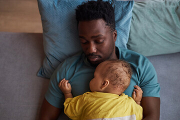 Top down portrait of young Black father with baby son falling asleep together at naptime
