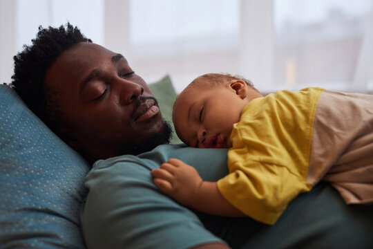 Side view portrait of exhausted young father falling asleep with cute little baby on chest
