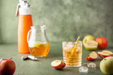 Apple juice and sparkling water in glass. Apfelschorle German drink. Apple fruit, ice and leaves in...
