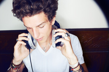 Man with headphones, rock dj and audio beats with rockstar attitude on white background with spotlight. Cool punk style, grunge sound and music, club culture with male model listening to earphones.