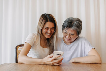 Asian Thai old mother and daughter using phone, both looking at tablet, watching and reading something with happy smiling, spending time together.