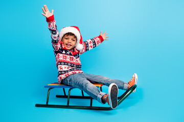 Full size photo of funky little kid wear red pullover jeans santa hat sitting on sleigh hands up...