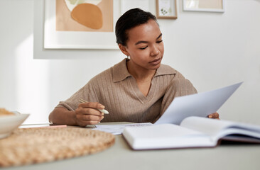 Minimal portrait of young Black woman reading document at home while studying or doing taxes, copy space