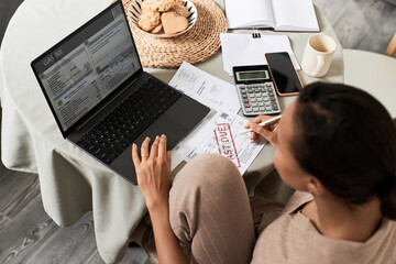 High angle portrait of Black young woman doing taxes at home and using laptop managing household