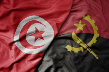 big waving national colorful flag of tunisia and national flag of angola .