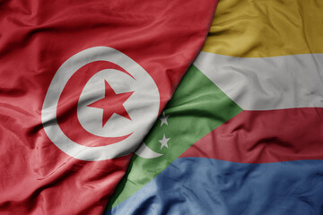 big waving national colorful flag of tunisia and national flag of comoros .