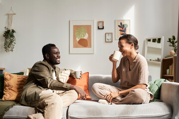 Side view portrait of young African American couple enjoying conversation sitting on comfortable...