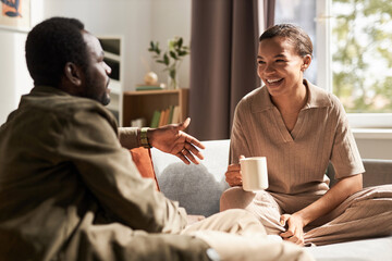 Portrait of young African American couple enjoying conversation in morning in cozy home, everyday...