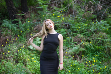 Young, beautiful blonde woman dressed in black walks through the forest in different postures and...