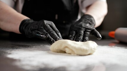 A man kneads dough in a pastry shop. Rolling out dough, close-up of a chef wearing gloves.