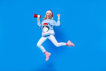 Obraz premium Full body cadre of jumping girl wearing ugly penguin ornament sweater hooray merry christmas proclaims isolated on blue color background