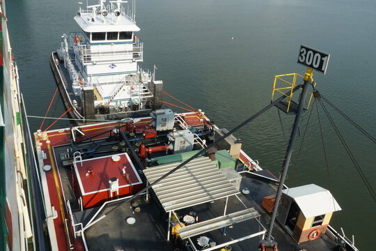 Houston, USA - 06 15 2023: Aerial view on tug boat with white superstructure and bunker barge with valves and manifolds alongside of the container vessel during transferring of fuel or bunkering. 