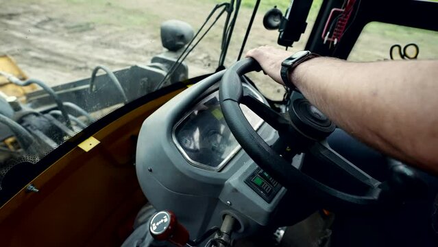 tractor driver sitting inside vehicle, closeup view of male hand on steering wheel