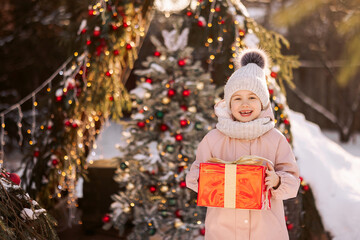 Little girl with a Christmas gift outdoors in winter on Christmas Eve. New Year background for holiday sale or promotion.