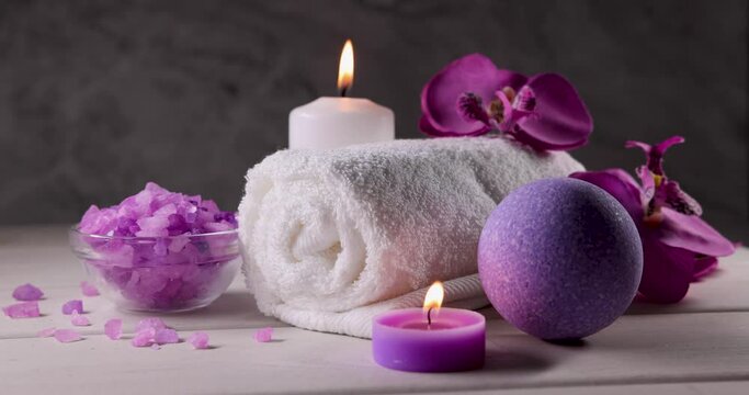 purple bath bomb, sea salt crystals, towel and burning scented candles on wooden table. body skin care. wellness spa