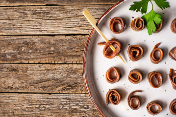 Cantabrian anchovies rolled and presented on a rustic plate, on an old wooden table, top view. Copy...