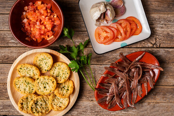 Cantabrian anchovies, toasted with parsley, chopped and sliced tomato and garlic, top view, rustic wood background.