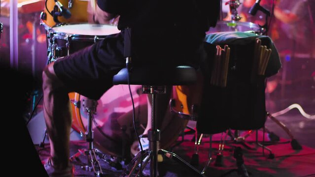 Close-up of drummer's feet pressing pedals of bass drum and hi-hat. Man playing drums fast at a concert. Rear view. Drummer on stage surrounded by lighting effects