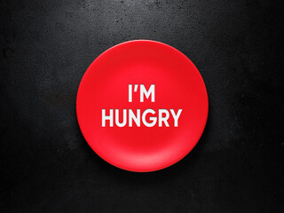 The inscription I am hungry on a red plate over black background. Hunger and dieting concept.