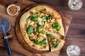 A spinach and pesto gourmet pizza hot out of the oven topped with basil.