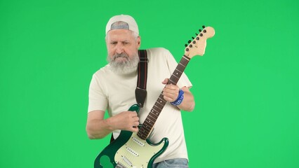 Obraz premium Portrait of senior man hipster on Chroma key green screen background, man in white t-shirt playing on electric guitar at camera. Advertising area, workspace mockup.