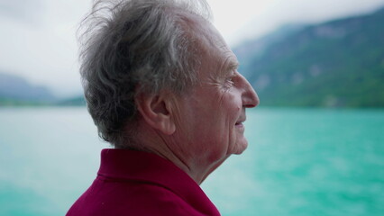 Carefree senior man enjoying serene nature's view of lake and mountains while traveling by boat,...