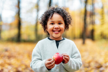 black child girl on maple leaves background holding apple
