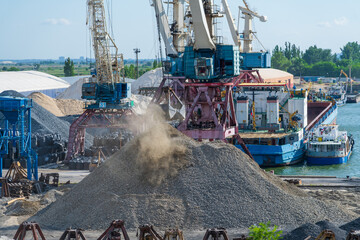 Close-up side view of level luffing bulk-handling crane unloading gravel using shell bucket in city...