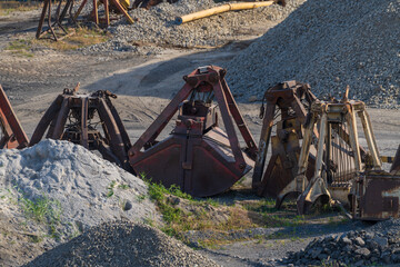 Close-up view of group of large shell buckets of bulk-handling crane lying on ground next to heaps of gravel in city port. Soft focus. Industrial machinery theme.