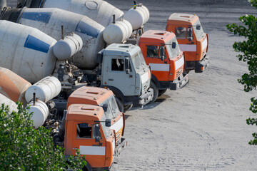 Close-up side view of group of concrete mixer trucks standing parked on ground in a sunny summer...