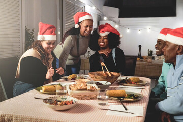 Happy African family celebrating Christmas dinner outside terrace house. Xmas holiday party and...