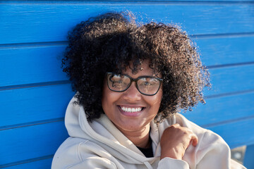 Black woman dressed in a beanie sweatshirt and afro hair on a blue background on a sunny day