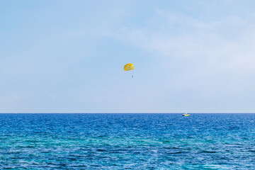 View of the sea with turquoise water and a yellow parasailing parachute being pulled by a...