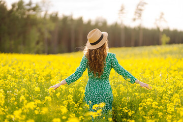 A happy woman in a hat walks through a blooming rapeseed field. Beautiful woman posing in a...