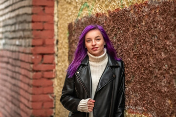 Portrait of a young beautiful girl with purple hair in a leather jacket in the autumn city.