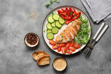 Grilled chicken breast with fresh vegetables on a gray concrete background. Top view, flat lay. Healthy dinner.