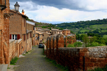 Photo of a street with stone houses with lanterns on one side and a stone wall on the other against...