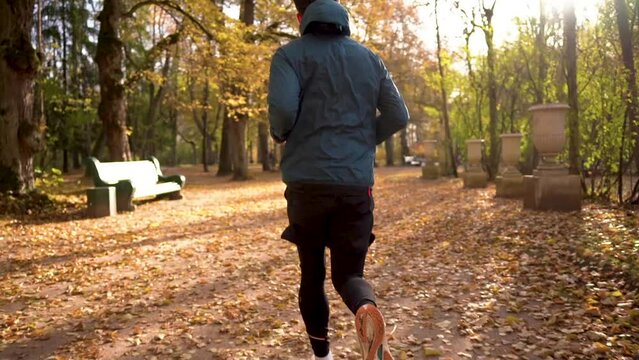 Runs takes steps jogging runner in the fall. Training of a male trainer to warm up the legs and body for running a long distance. A man in warm sports clothes for winter training.