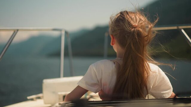 Little girl wearing scoliosis brace enjoys tourist boat rocking on ocean bay waves backside view. Child with back disease travels by yacht across sea