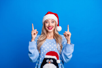 Obraz premium Photo portrait of pretty blonde young girl excited finger point up dressed penguin sweater x-mas hat isolated on blue color background