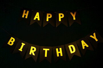 Against the background of a dark wall there is an inscription in golden letters happy birthday