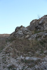 A rocky hill with grass and a blue sky