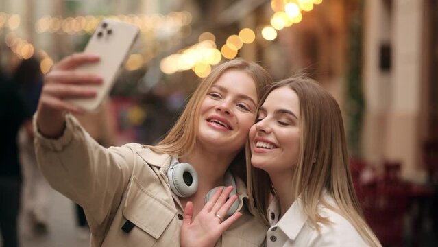 Pretty young women friends taking selfie photograph saving great memories on smartphone mobile phone at sunny city centre Pretty girls create content for social media together outdoors