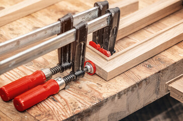 Carpenter clamps are fixed to boards. Gluing joinery in workshop - obrazy, fototapety, plakaty