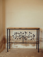 A vertical close-up of a table in an abandoned villa in Porto Cervo showcases a captivating combination of rustic elegance with its wooden top, metal legs, and a striking metal tree-shaped ornament.