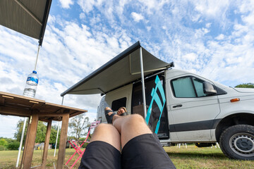 Beine in Sandalen entspannen vor einem Camper auf einem Stuhl auf einem Campingplatz